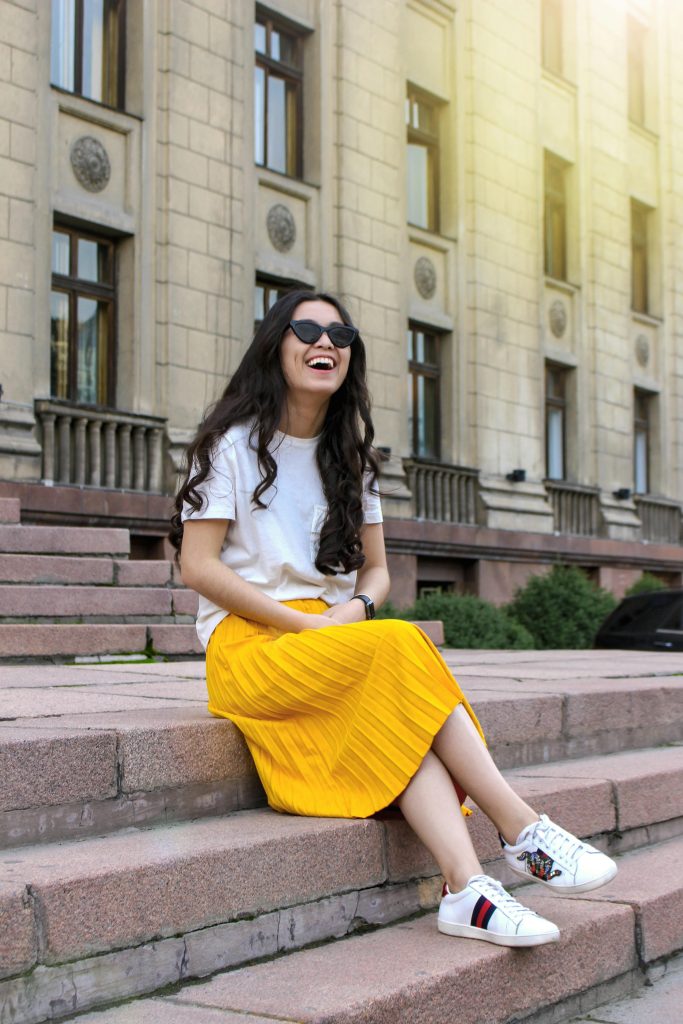 Smiling young woman in a yellow skirt sitting on steps in Almaty, Kazakhstan.